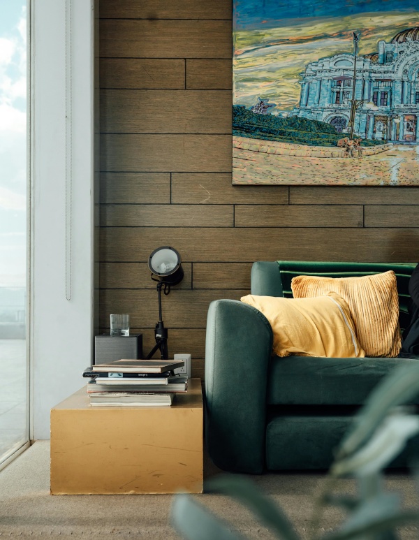 A stylish living room with a large window, wood-paneled wall with artwork, and a couch